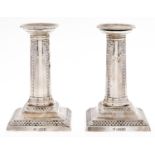A pair of Edwardian silver dwarf columnar candlesticks, stamped with festoons and bows, nozzles,