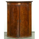 A George III bow fronted mahogany hanging corner cupboard, early 19th c, with harewood ground