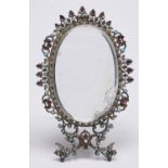 An oval giltmetal and 'jewelled' strut mirror, early 20th c, bevelled plate, 17cm h Silvering of