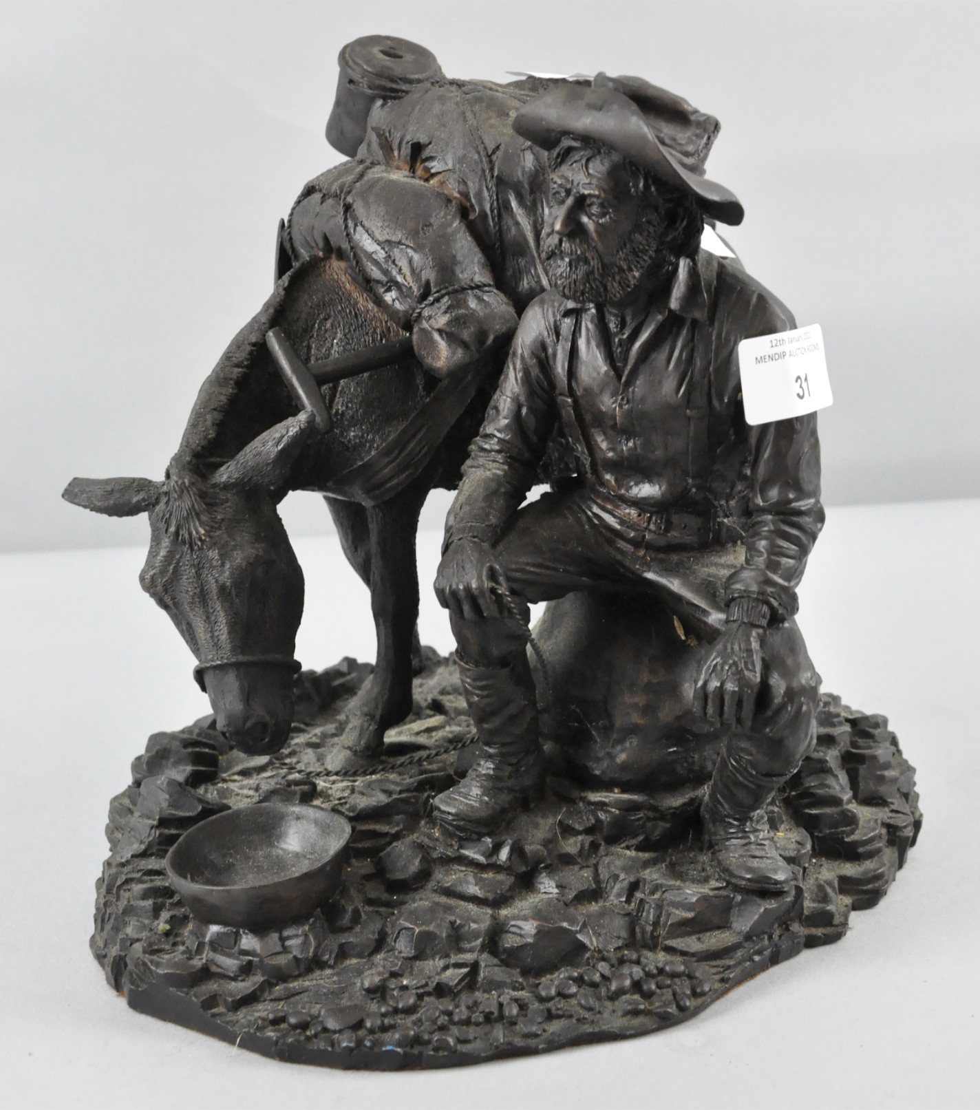 A Bronzed resin style sculpture of a Prospector taking a rest and feeding his donkey,