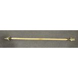 A decorative curtain pole in the form of an arrow with brass finial ends,