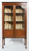 An Edwardian mahogany display cabinet inlaid with ribbon detailing, raised on four feet,