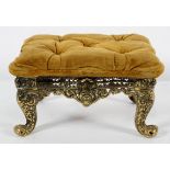 A brass footstool with buttoned upholstery, pierced decoration on scrolling legs,