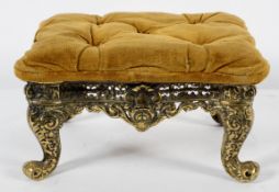 A brass footstool with buttoned upholstery, pierced decoration on scrolling legs,