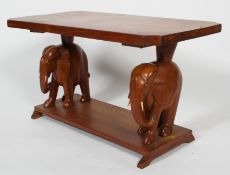 A hardwood elephant table, the shaped rectangular top on a pair of African elephant supports,