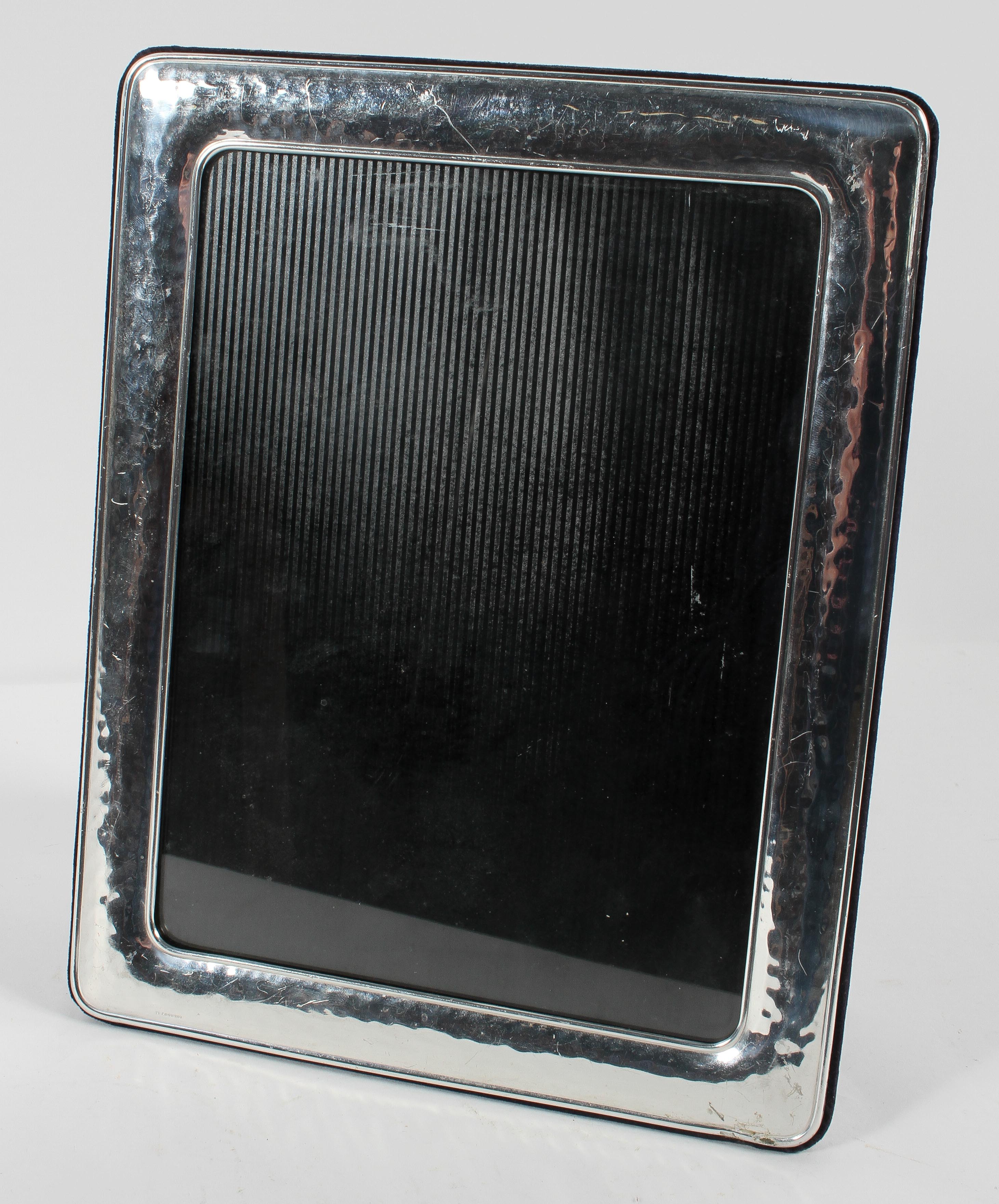 A white metal photo frame of rectangular cushion form with planished decoration.