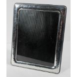 A white metal photo frame of rectangular cushion form with planished decoration.