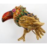 A yellow metal brooch in the style of a bird with enamelled finish and ruby set eye.