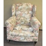 A wing back armchair, raised upon wooden feet,