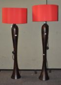A pair of modern standard lamps, of flowing form with large red shades,