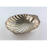 A George V silver butter dish, of shell form, raised upon three ball feet,