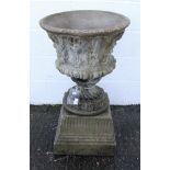 A reconstituted stone garden urn with foliate swag decoration on a socle base and square section