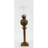 A brass oil lamp, the glass shade and flue above a repousse reservoir and Corinthian column base,