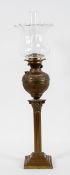 A brass oil lamp, the glass shade and flue above a repousse reservoir and Corinthian column base,