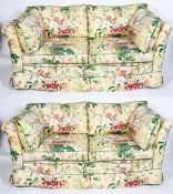 A pair of modern sofas with floral upholstery on loose cushions, a geometric fabric beneath,