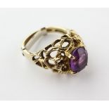 A yellow metal single stone ring of abstract design set with an oval faceted cut amethyst