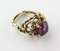 A yellow metal single stone ring of abstract design set with an oval faceted cut amethyst