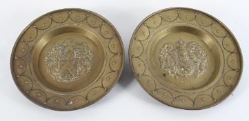 A pair of brass Heraldic chargers, each with an Armorial crest inside a swagged border,
