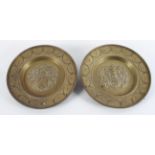 A pair of brass Heraldic chargers, each with an Armorial crest inside a swagged border,