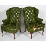 A pair of George II style wing back arm chairs, with green leather buttoned upholstery,