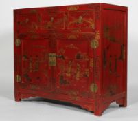 A Chinese red lacquered and gilt side cabinet, with three drawers above a pair of cupboard doors,