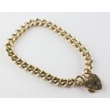 A yellow metal curb link bracelet with padlock and safety chain. Hallmarked 9ct gold, Birmingham.