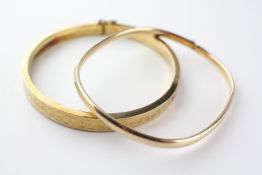 A collection of two yellow metal hollow bangles with engraved design.