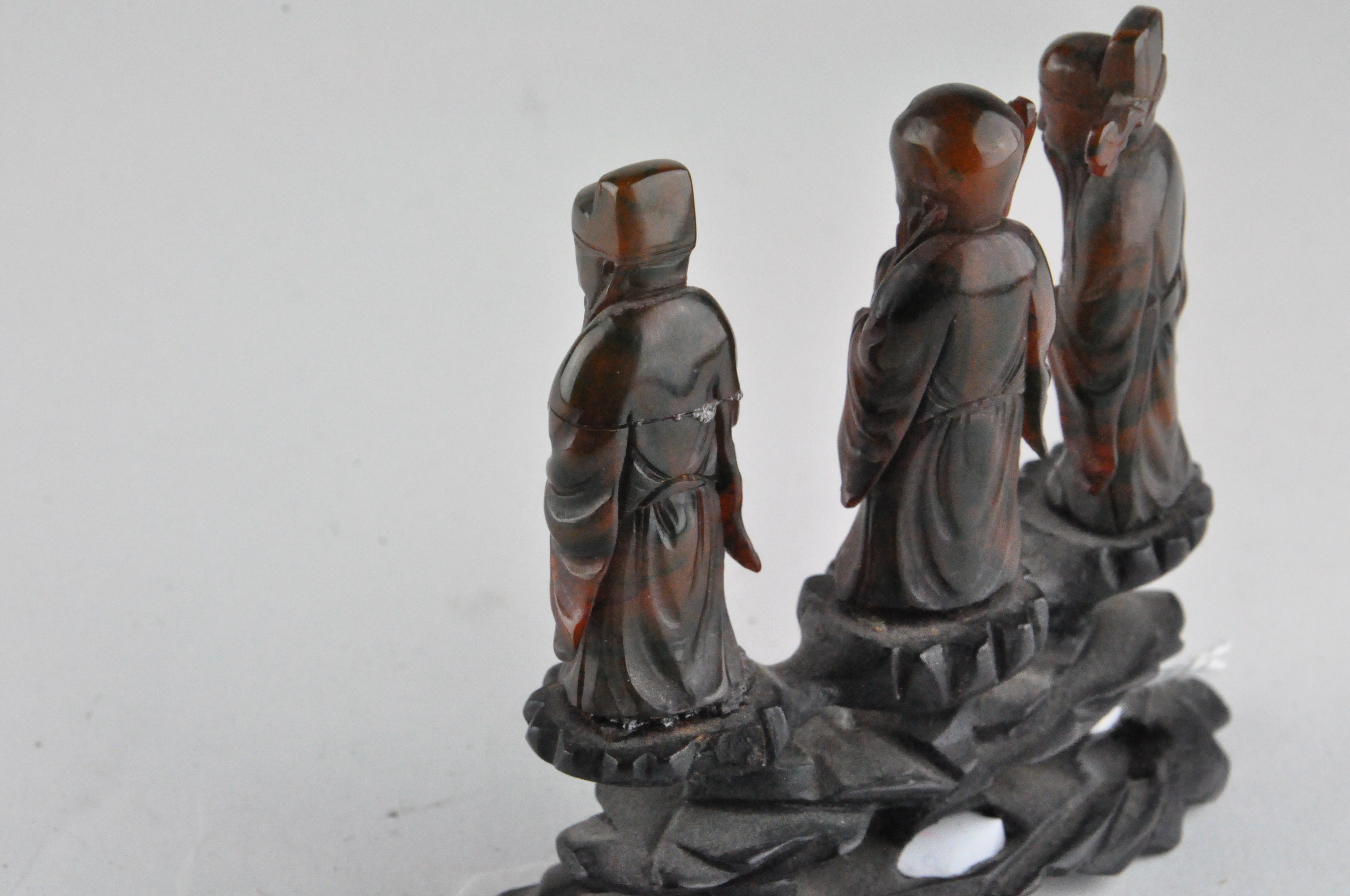 A group of three Chinese amber style figures of Immortals, standing on a carved wood base, - Image 4 of 9