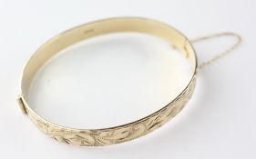 A yellow metal half engraved hinged bangle with slide clasp and safety chain.