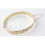 A yellow metal half engraved hinged bangle with slide clasp and safety chain.