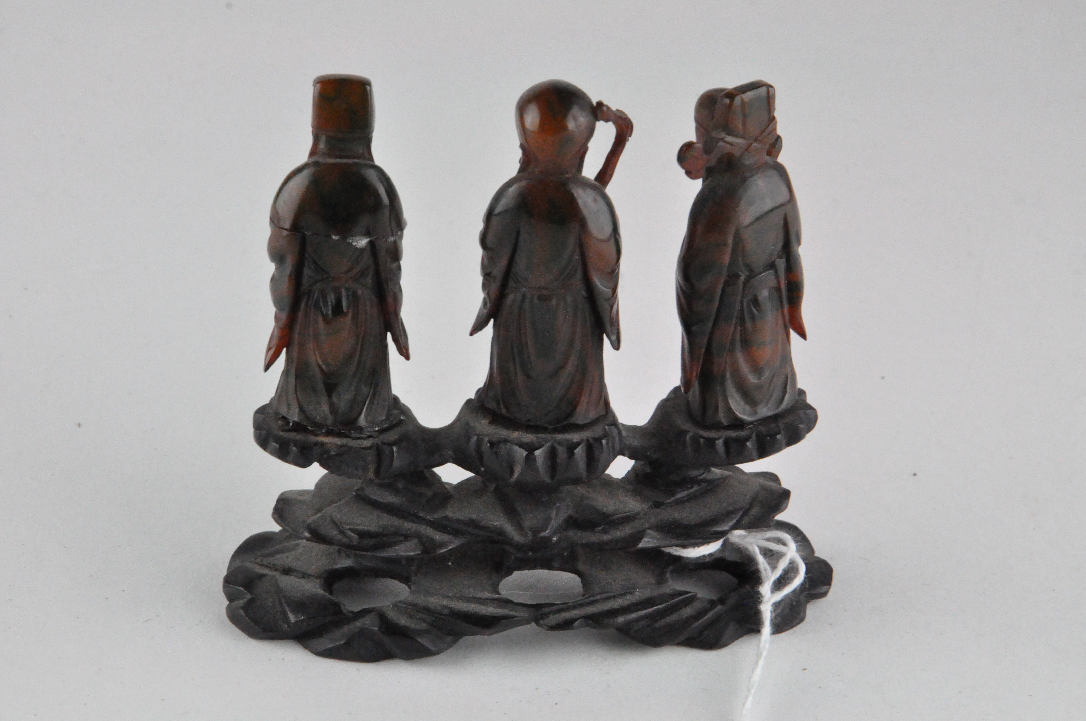 A group of three Chinese amber style figures of Immortals, standing on a carved wood base, - Image 6 of 9