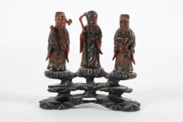 A group of three Chinese amber style figures of Immortals, standing on a carved wood base,