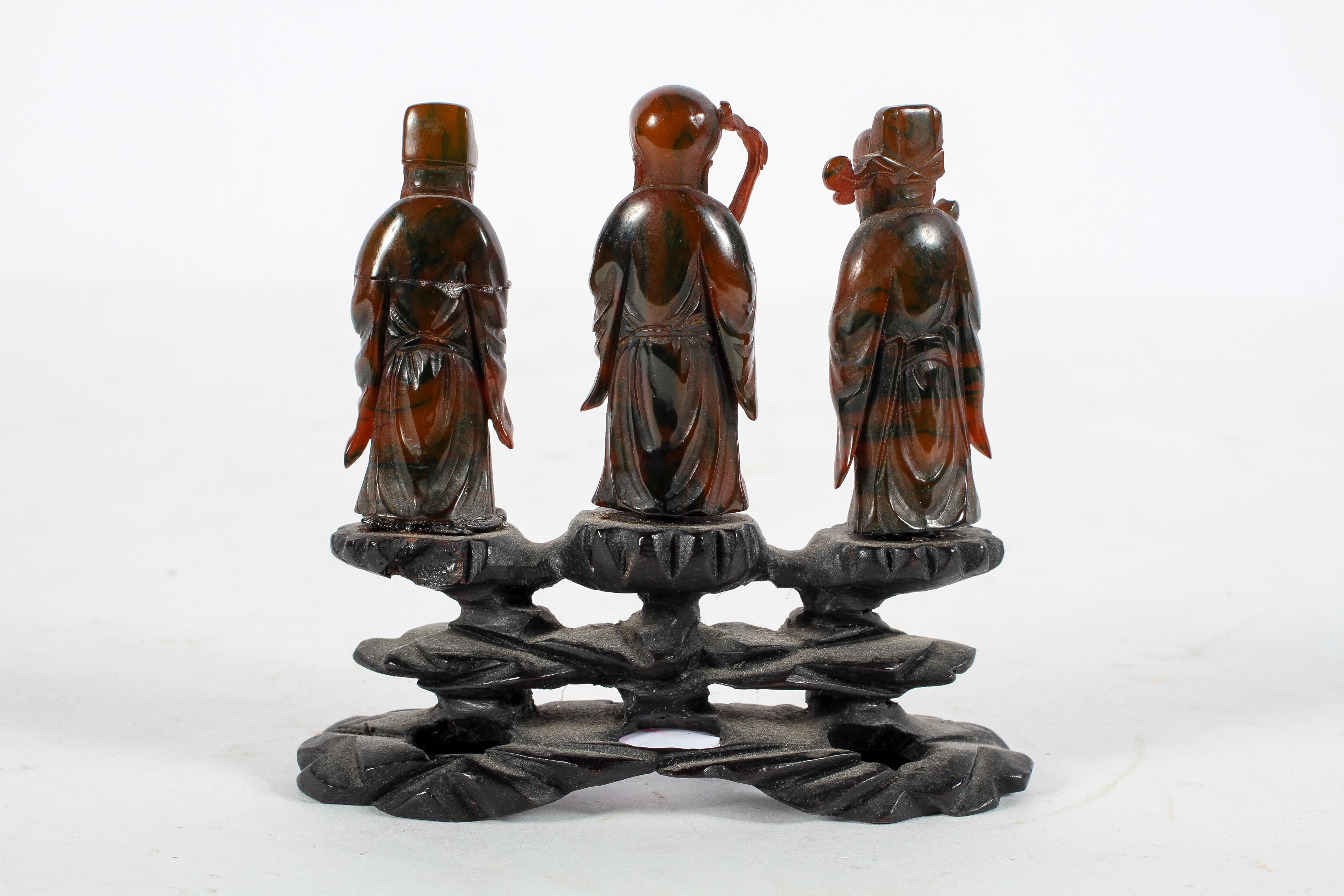 A group of three Chinese amber style figures of Immortals, standing on a carved wood base, - Image 2 of 9