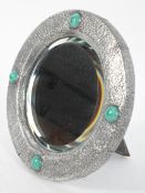 An Arts and Crafts circular polished metal mirror, applied with four glazed ceramic cabochons,