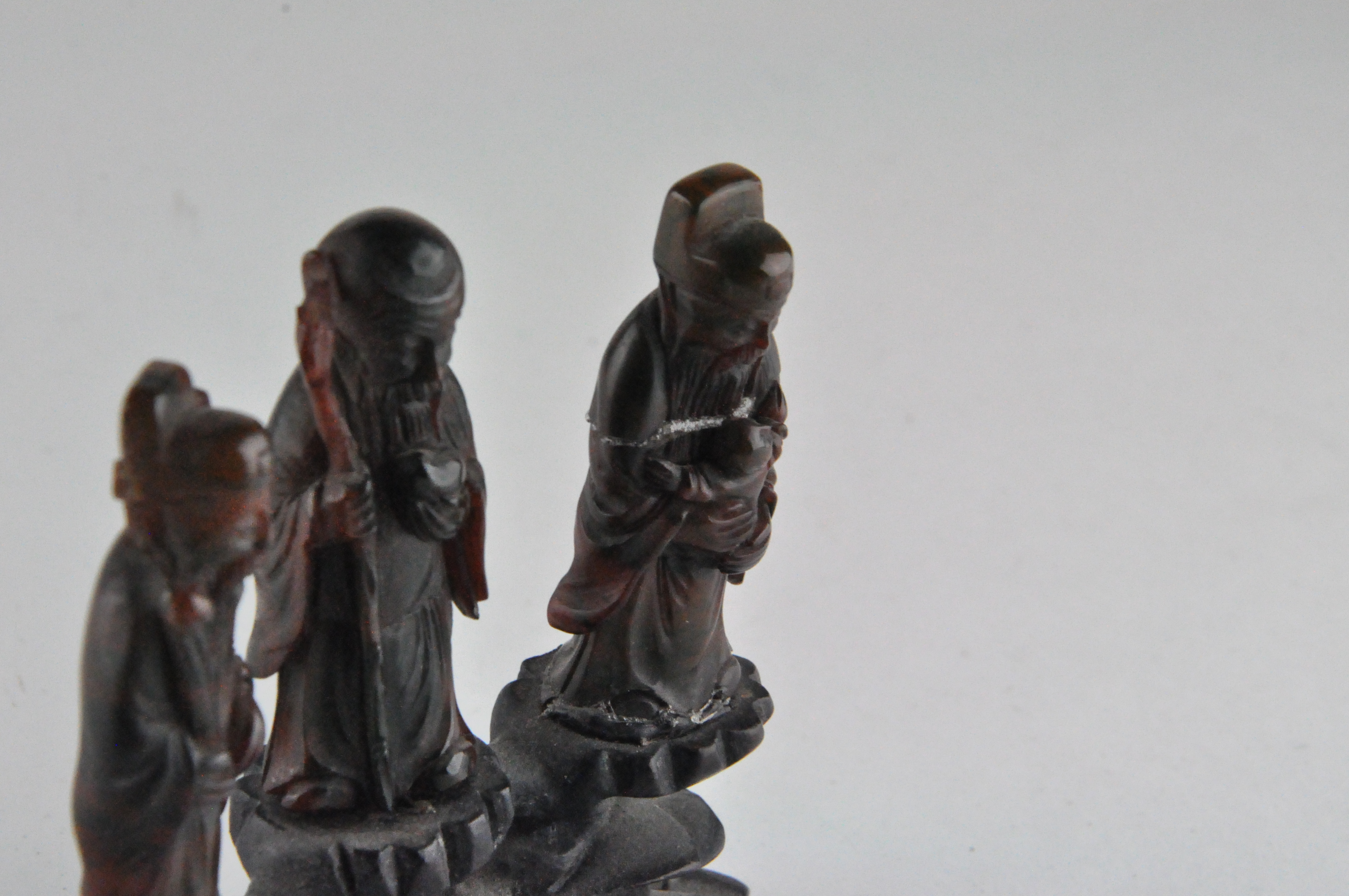 A group of three Chinese amber style figures of Immortals, standing on a carved wood base, - Image 3 of 9