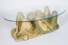 A novelty coffee table, the oval glass top supported on a plaster group of an entwined couple,