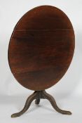 A George III elm and oak tilt top table, the circular top on a baluster column and tripod base,