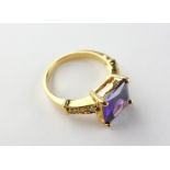 A yellow metal dress ring set with purple and white stones. Tested as gold plated. Size O 6.