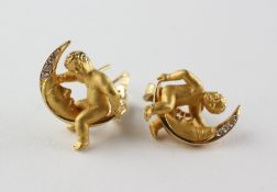 A yellow metal pair of earrings stylized as a cherub and moon