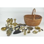 A wicker basket containing an assortment of metalware, including horse brasses, ash trays,