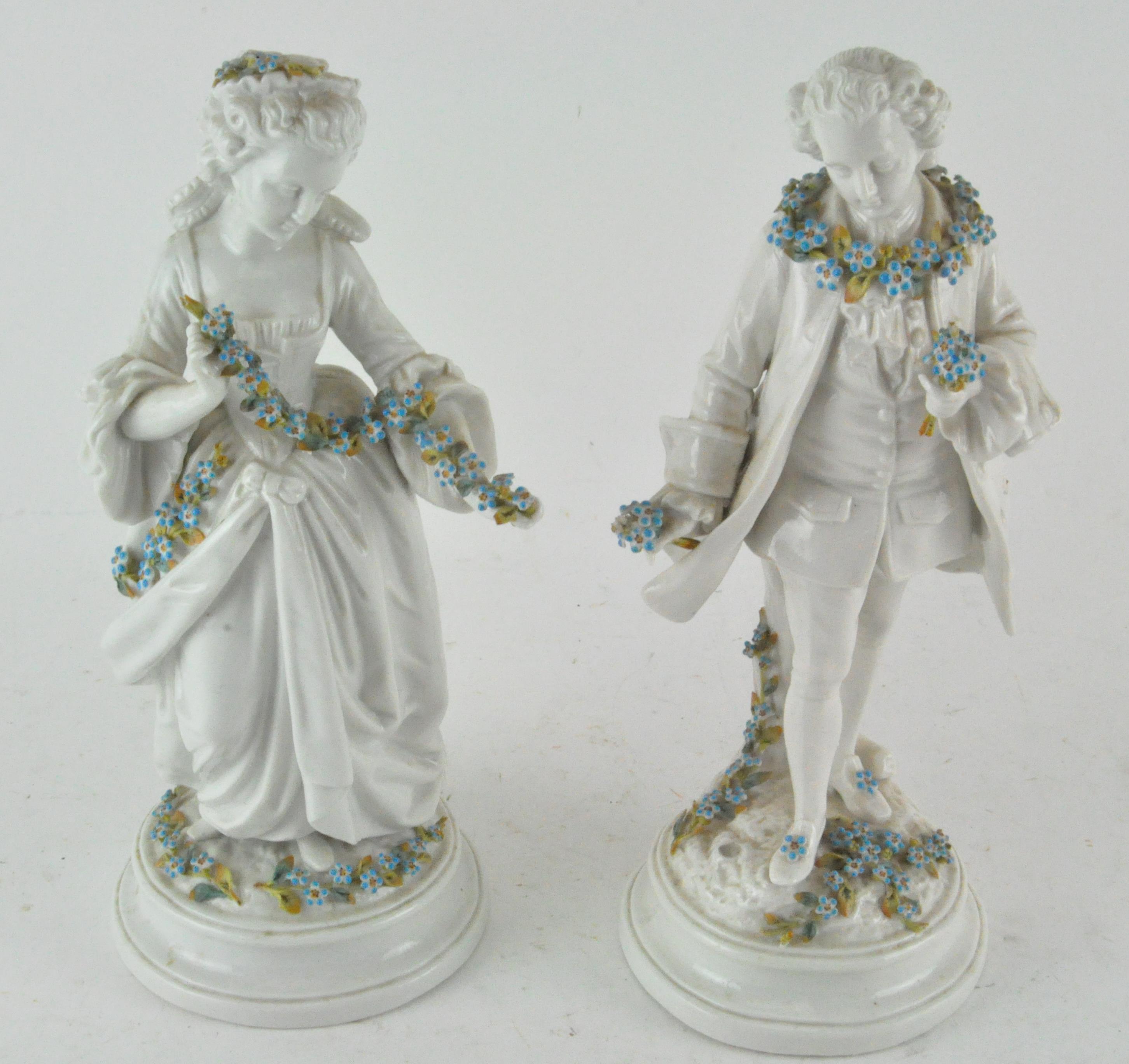 A pair of male and female porcelain figures, holding garlands of...