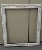 A large white painted picture frame with highly detailed decoration adorning the border,