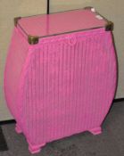 A vibrant pink Lloyd Loom laundry basket with fitted glass top,