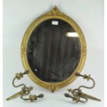 An ornate gilt framed mirror of oval form, 58cm x 45cm; together with a pair of brass wall lights,
