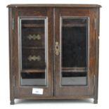 An early 20th century oak smoker's cabinet, the two doors with bevelled edged glass panels,