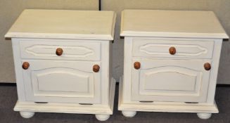A pair of white painted bedside cabinets, each with a single drawer over a drop front cupboard,