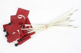 A collection of nine numbered ski flags, each white metal pole with red flag with black ball finial,