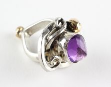 A large white metal ring of abstract design principally set with a faceted cut amethyst .