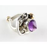 A large white metal ring of abstract design principally set with a faceted cut amethyst .