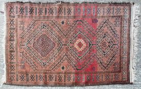 A Persian village rug, with three hooked medallions on an abrashed red ground,